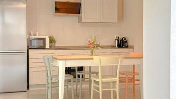Una cocina equipada con refrigerador, microondas, gabinetes, cafetera y una mesa con sillas.