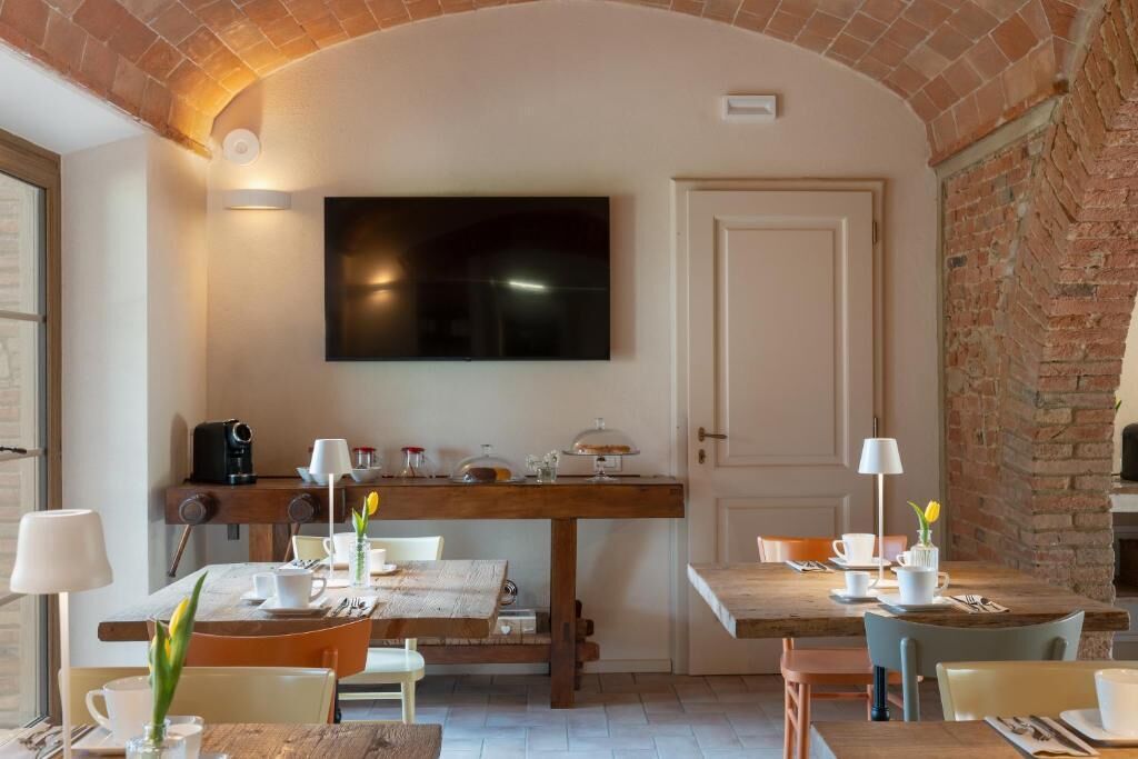 Un área de comedor con pared de ladrillo, un televisor de pantalla plana sobre una mesa de madera, y una puerta a la derecha.