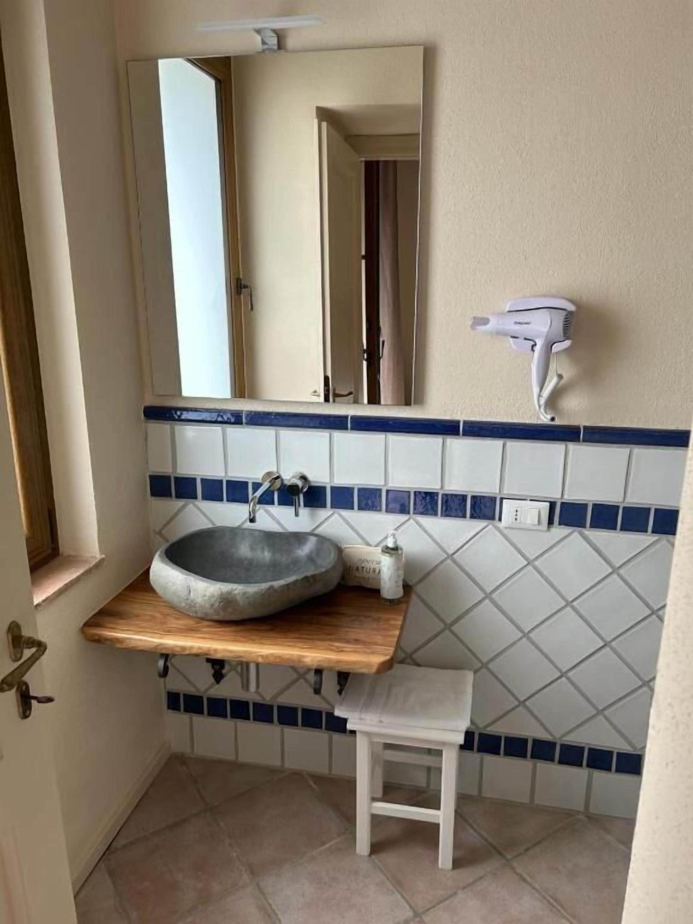 A bathroom with a wooden vanity, a round sink, a mirror, and a hairdryer mounted on the wall.
