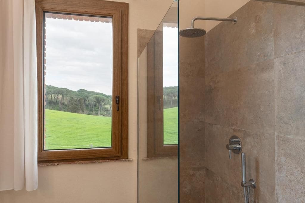 Un baño con ducha, una ventana que da a un campo verde y una puerta.
