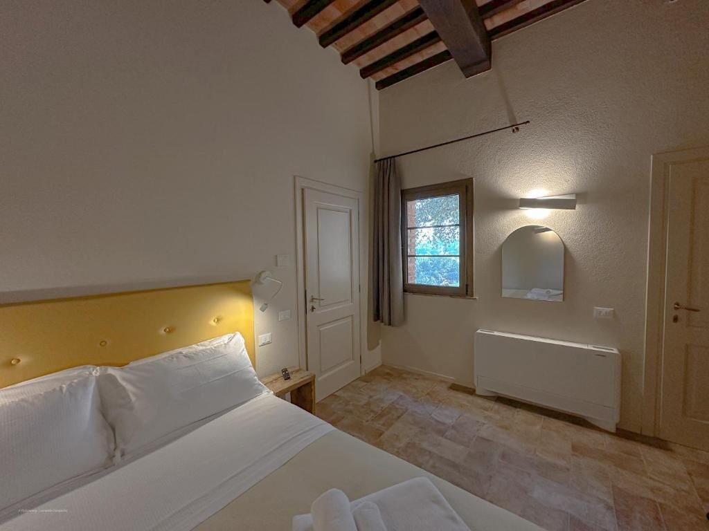 A bedroom with a bed, a nightstand, a window, a radiator, and a door.