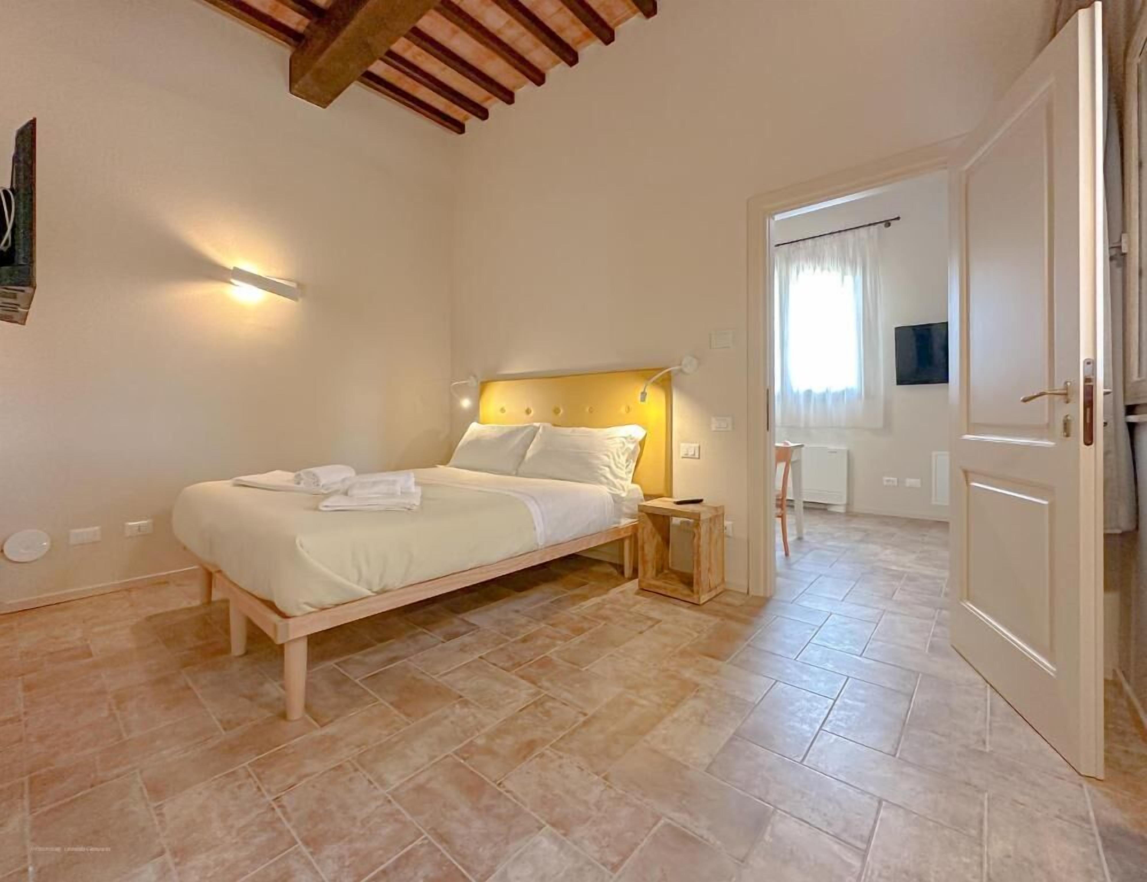 Quarto com cama, mesa de cabeceira e porta para outro cômodo.