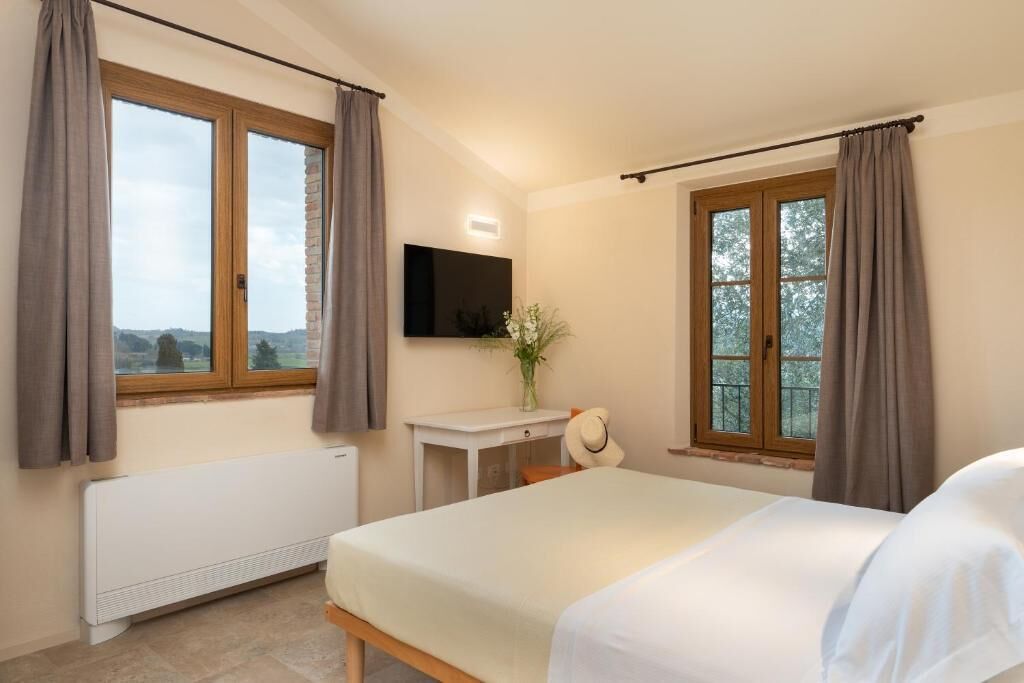 A bedroom with a bed, a desk, a chair, a TV, and a window with curtains.
