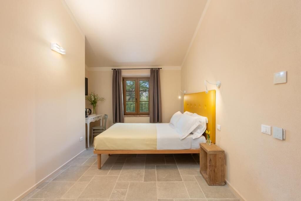 A bedroom with a bed, bedside table, lamp, and window with curtains.