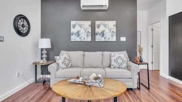 A living room with a grey sofa, round coffee table, and two wall-mounted air conditioning units.
