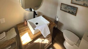 Un bagno con un mobile contenitore in legno, uno specchio rotondo, un lavandino bianco e un water.
