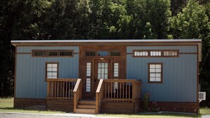 Una piccola baita di legno con un portico, due finestre laterali e una porta con un piccolo oblò sopra.
