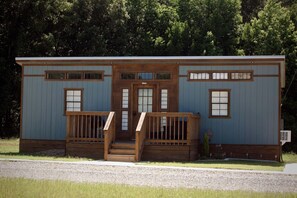 A small wooden cabin with a front porch, two windows on the side, and a door with a small window above it. - Suzy Two — Cozy Queen Suite Near MSU (Starkville)