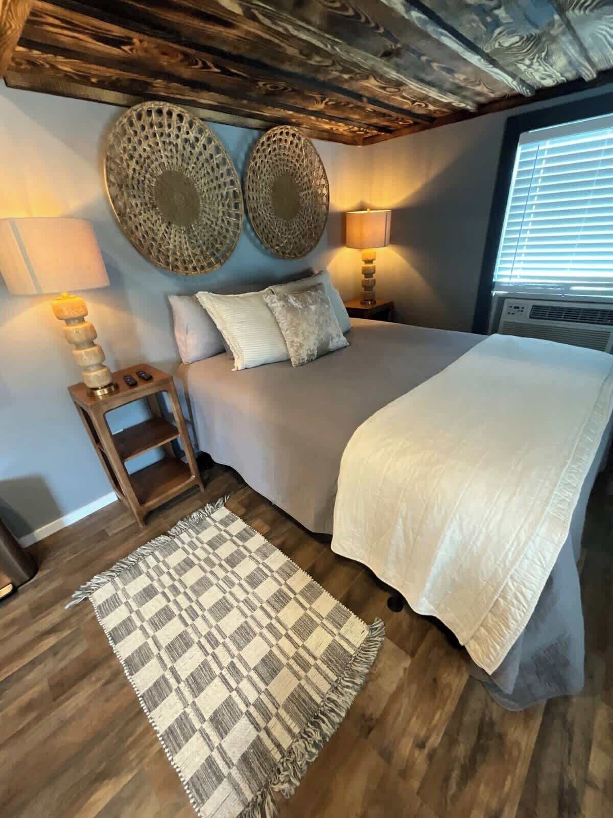 Une chambre à coucher avec un lit, des lampes de chevet, un tapis à motifs et des œuvres d’art décoratives accrochées au mur.