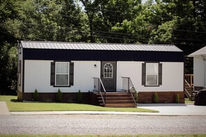 A small, single-story house with a front porch, a door with a window, and a small set of stairs leading up to the entrance. - Suzy Blue — Cozy Queen Cottage Near MSU (Starkville)