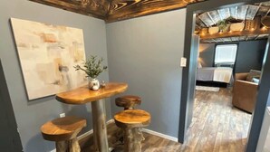 Una habitación con techo de madera, una mesa de comedor con taburetes, un cuadro en la pared y vistas a otra habitación.