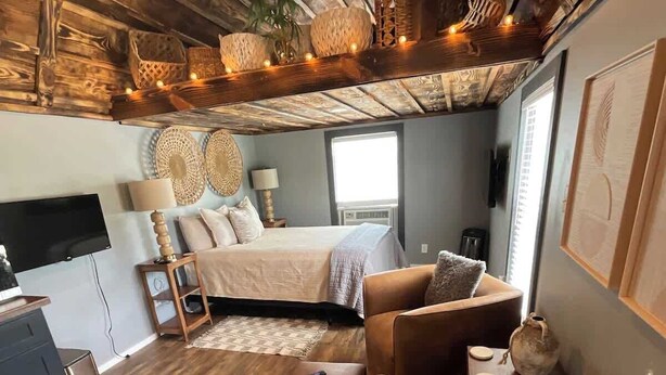 Una habitación acogedora con cama, sofá, televisor y techo de madera.