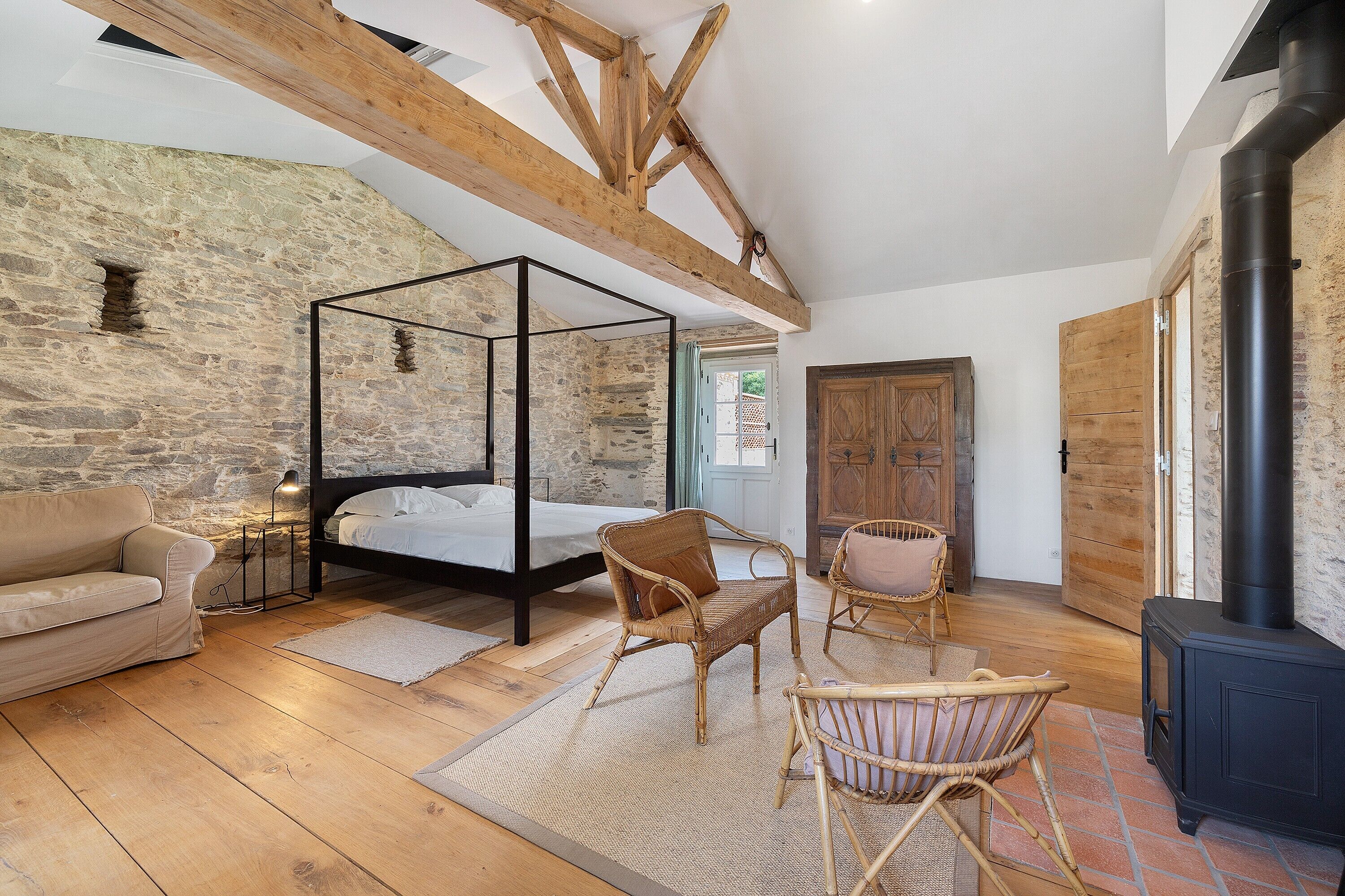 Une chambre dotée d’un lit à baldaquin, d’un plancher en bois, de murs en pierre et d’une cheminée.