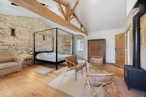 A room with a four-poster bed, wooden flooring, stone walls, and a fireplace.