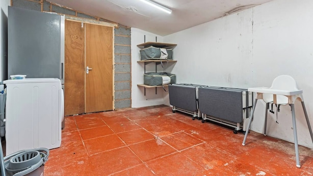 Um quarto com um radiador branco, uma porta de madeira, uma cadeira branca e um chão ladrilhado.