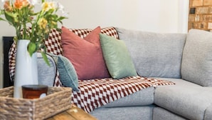 Um sofá cinzento com almofadas decorativas estampadas e um vaso de flores sobre uma mesa de madeira.