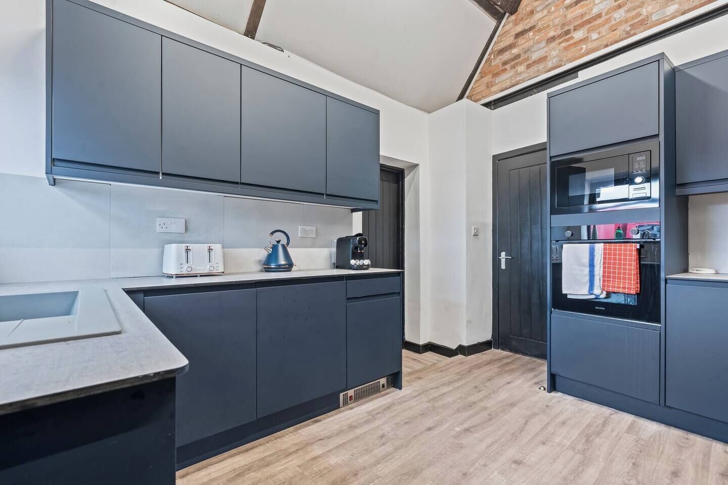 A modern kitchen with grey cabinets, a built-in oven, and a kettle on the counter.