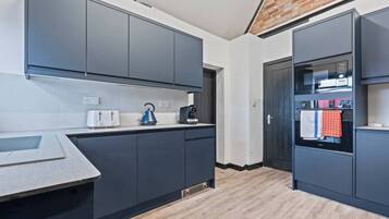 A modern kitchen with grey cabinets, a built-in oven, and a kettle on the counter.