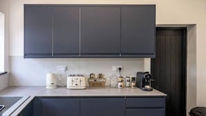 Cozinha compacta com armários escuros, uma torradeira, uma cafeteira e potes na bancada.