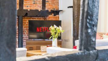A brick fireplace with a flat-screen TV displaying 'NETFLIX' and a vase with flowers on a wooden table.