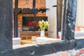 Ein Kamin aus Ziegelsteinen mit einem Flachbildfernseher, der 'NETFLIX' anzeigt, und eine Vase mit Blumen auf einem Holztisch.