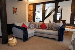 A living room with a grey sofa, red and plaid cushions, a woven basket, and exposed brick walls.
