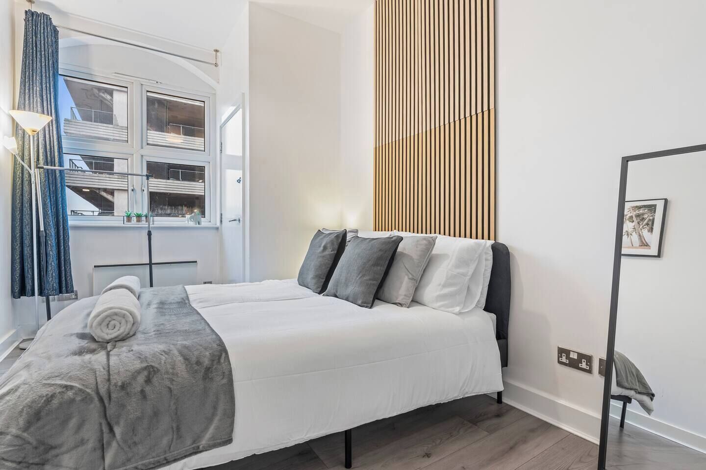 A hotel room with a bed, a window, a curtain, a wall-mounted light fixture, and a picture frame.