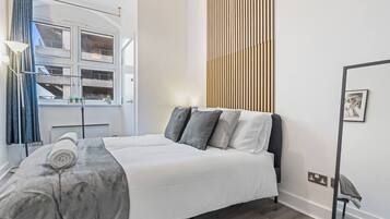A hotel room with a bed, a window, a curtain, a wall-mounted light fixture, and a picture frame.