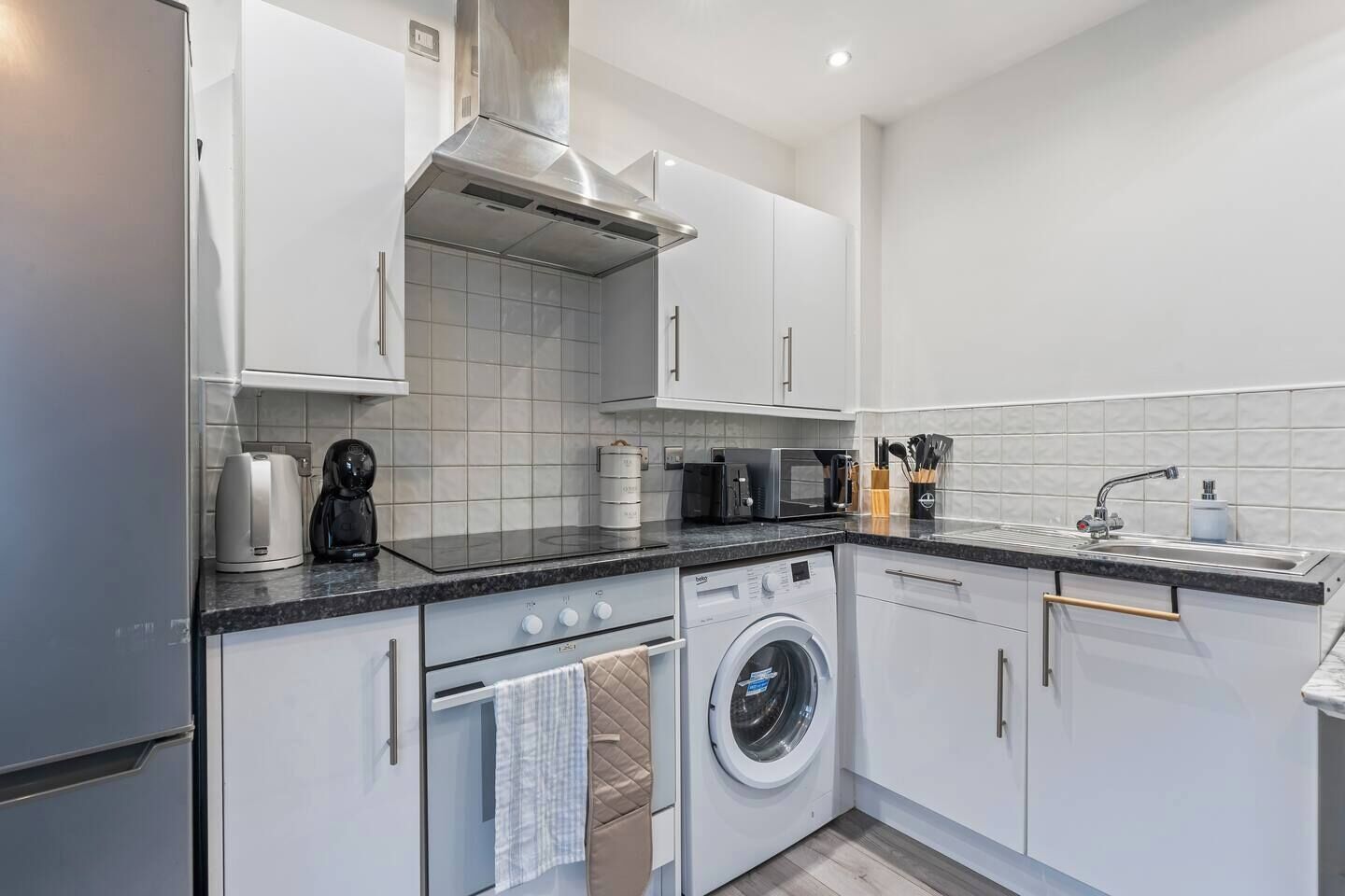 A modern kitchen with white cabinets, a built-in oven, a microwave, a coffee maker, and a washing machine.