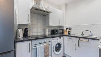 A modern kitchen with white cabinets, a built-in oven, a microwave, a coffee maker, and a washing machine.