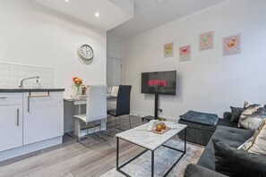 Un saló modern amb un sofà, una taula de centre, un televisor de pantalla plana i una zona de menjador amb taula i cadires.