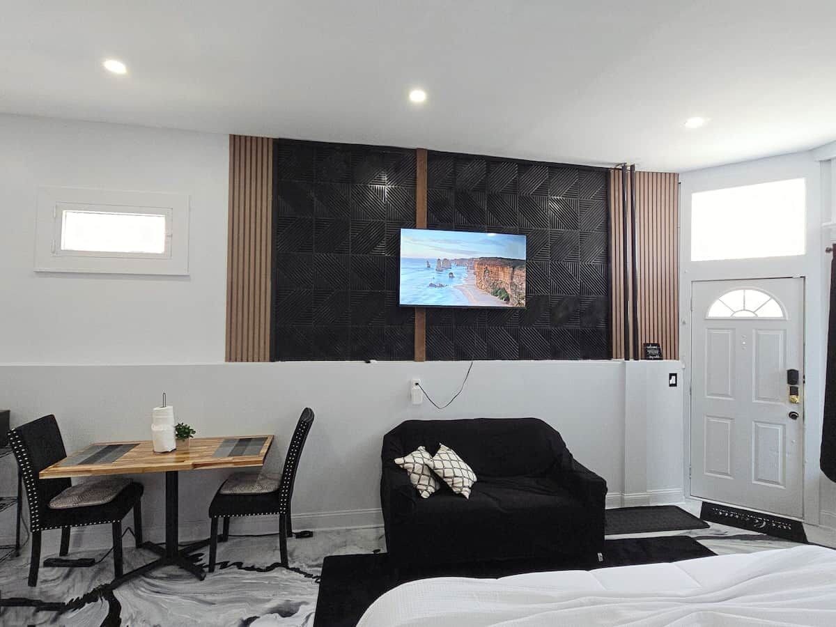 A hotel room with a bed, a TV mounted on the wall, a dining table with chairs, and a black sofa.