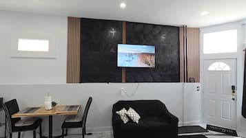 A hotel room with a bed, a TV mounted on the wall, a dining table with chairs, and a black sofa.