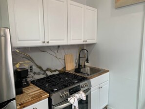 Een keuken met witte kastjes, een roestvrijstalen fornuis, een spoelbak en een koffiezetapparaat.