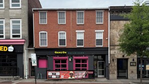 Ein Gebäude mit einer Schaufensterfassade, auf der 'GAMEON bar+arcade' steht, und ein Schild für 'GREEN' auf der gegenüberliegenden Straßenseite.