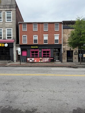 A building with a storefront labeled 'GAMEON bar+arcade' and a sign for 'GREEN' across the street. - Modern Fed Hill studio: steps to pubs/city vibes! (Baltimore)