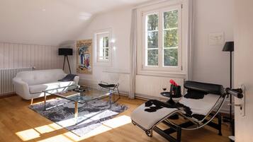 Ein modernes Wohnzimmer mit einem weißen Sofa, einem Glastisch, einem schwarz-weißen Sessel und einem großen Fenster, das für natürliches Licht sorgt.