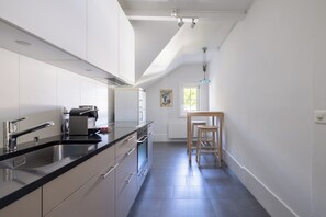 Una cocina moderna con encimera negra, electrodomésticos de acero inoxidable y una silla de madera.