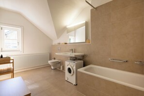Et moderne badeværelse med vaskemaskine, toilet, håndvask og badekar.