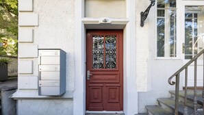 Punainen ovi, jossa on koristeellinen lasipaneeli, postilaatikko ja portaat, jotka johtavat valkoiseen rakennukseen, jossa on ikkuna.