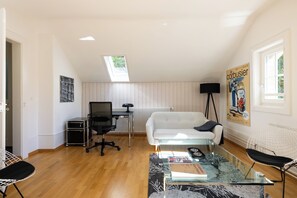 Un espacio habitable compacto con cama elevada, escritorio pequeño, sofá y mesa de centro de vidrio.