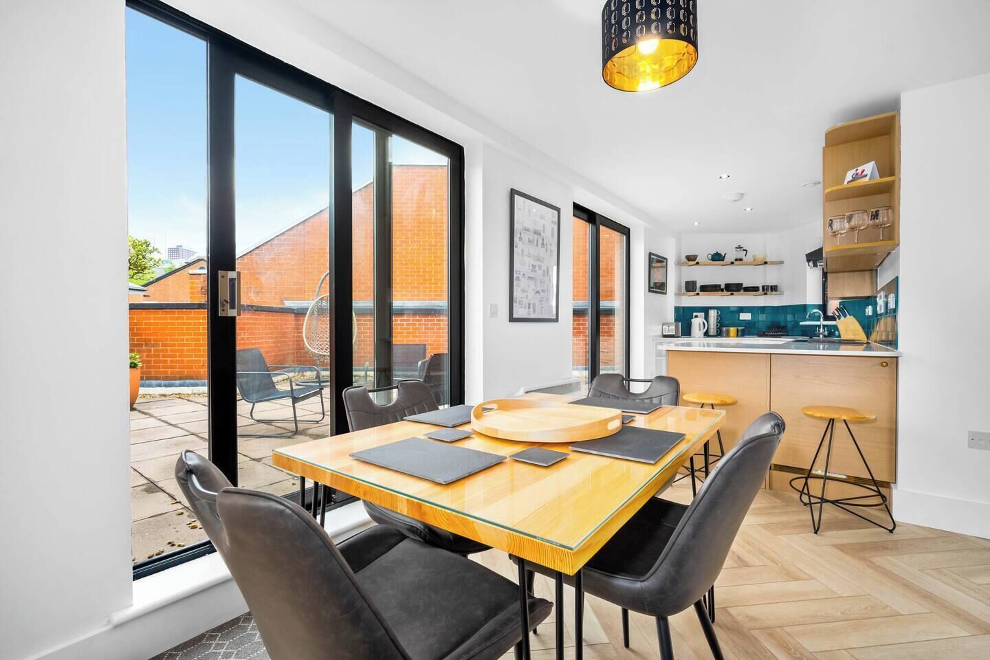 A modern kitchen with a central island, a dining area with a large table and chairs, and a view of a brick building outside.