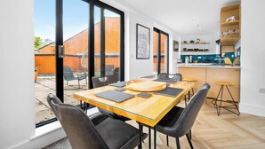 A modern kitchen with a central island, a dining area with a large table and chairs, and a view of a brick building outside. - #116 Modern 2 bed - 10 mins from Bullring & Grand Central (West Midlands)