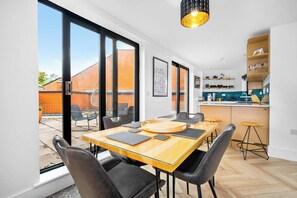 Eine moderne Küche mit einer zentralen Kochinsel, einem Essbereich mit großem Tisch und Stühlen und Blick auf ein Backsteingebäude.