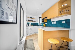 Une cuisine moderne avec des meubles blancs, un pare-feu turquoise et un coin bar avec des tabourets.