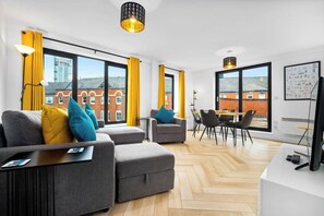 Ein modernes Wohnzimmer mit einer Sofagarnitur, einem Essbereich und großen Fenstern mit Vorhängen.