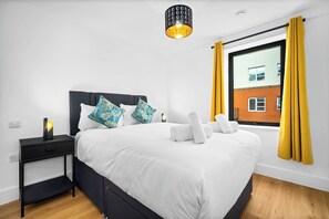 A modern bedroom with a bed, pillows, a nightstand, a lamp, and a window with curtains.