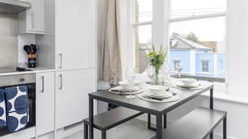 Een moderne keuken met witte kasten, een inbouwoven en een eettafel voor vier personen, gedekt met witte borden en glazen.