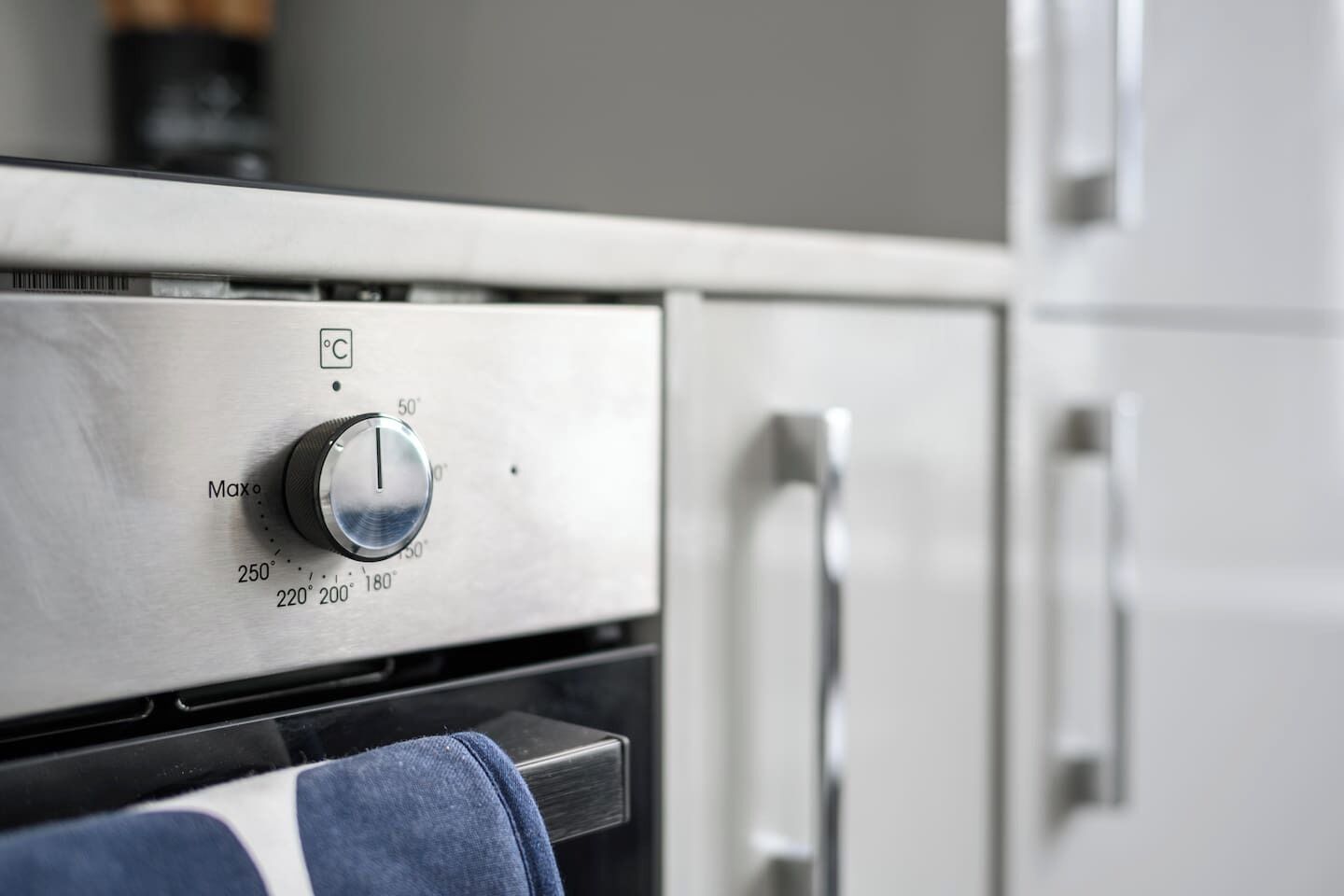 A kitchen with a stainless steel oven, a temperature control knob, and a blue towel hanging on the oven door handle.
