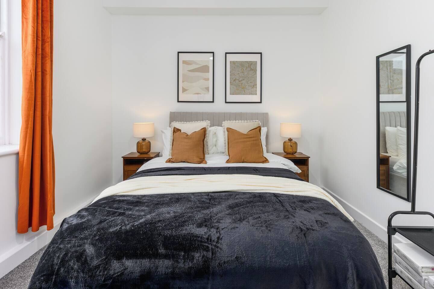 Een hotelkamer met een bed, twee nachtkastjes, een spiegel en een raam met gordijnen.